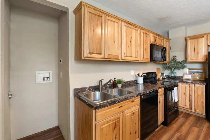 West unit. Kitchen featuring wood-finish cabinetry, dark countertop surfaces, stainless steel double basin sink, and black appliances