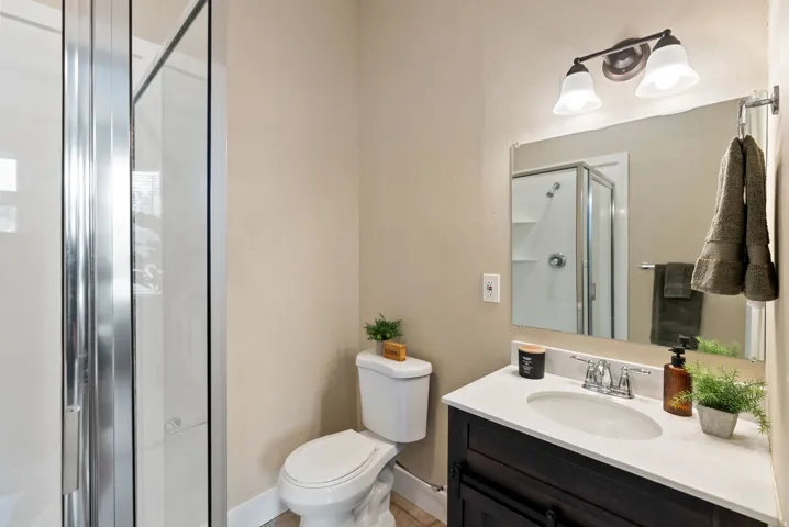 West unit. Bathroom featuring a glass-enclosed shower, a vanity with a white countertop, a dark wood-finish cabinet, and a wall-mounted light fixture