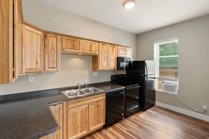 East unit. Kitchen featuring natural wood cabinetry, dark speckled countertops, and a double basin stainless steel sink