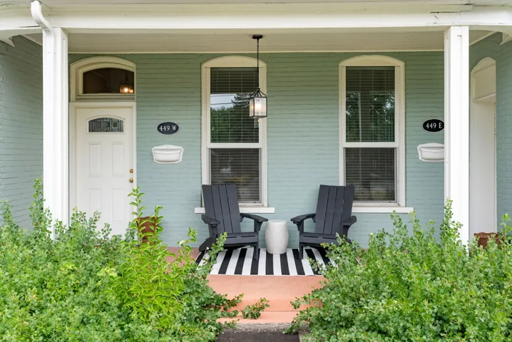 Inviting covered porch featuring a white entry door with an arched transom, painted brick exterior, and white trim