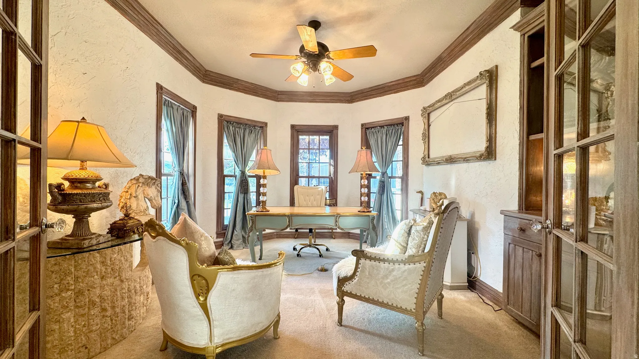 Formal room featuring textured walls, multiple windows, a ceiling fan, and built-in wood cabinetry with glass doors