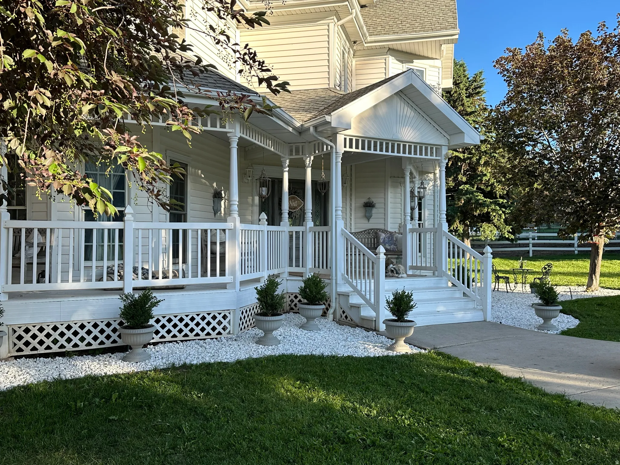 Inviting Victorian-style front porch with white railings and lattice skirting, featuring a gabled entryway and exterior wall sconces