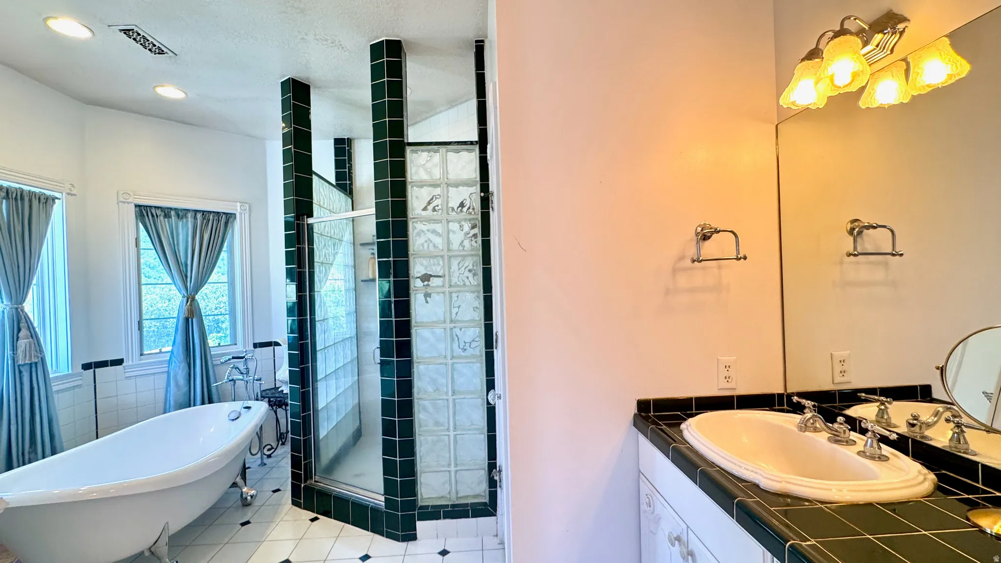 Bathroom featuring a freestanding clawfoot tub, a walk-in shower with glass block walls and dark green tile accents, and a vanity with a drop-in sink and dark green tile countertop