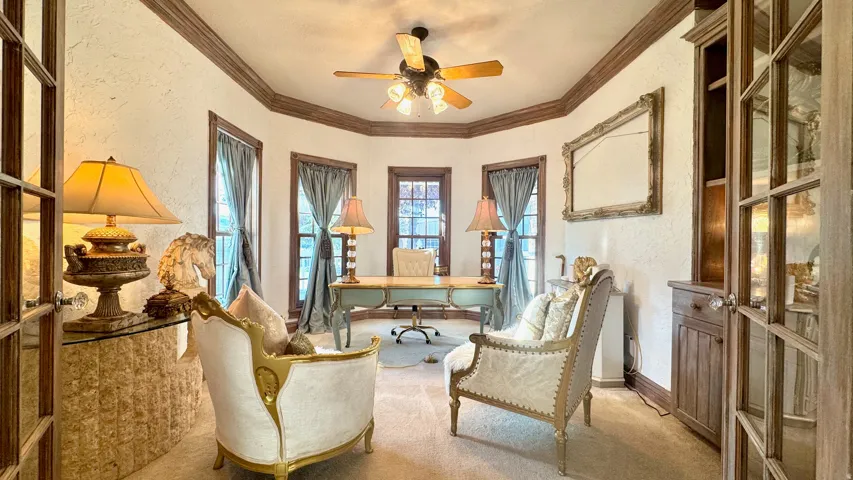 Formal room featuring textured walls, multiple windows, a ceiling fan, and built-in wood cabinetry with glass doors