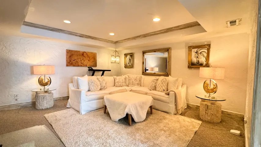Recessed lighting illuminates a spacious room featuring textured white walls and contrasting ceiling details