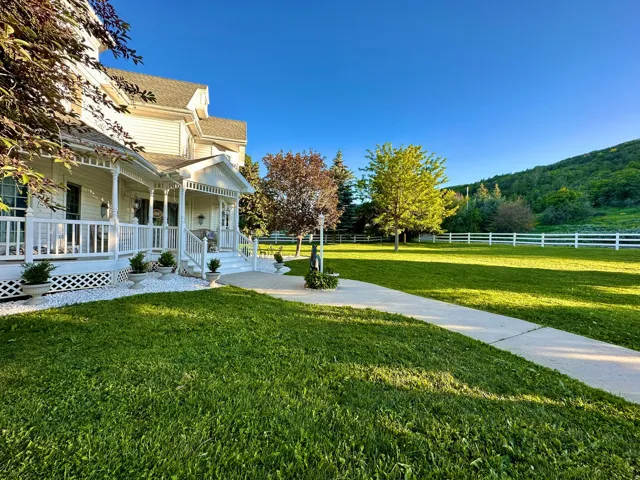 White vinyl siding residence featuring a wraparound porch with white railings, a concrete pathway, and a sprawling green lawn