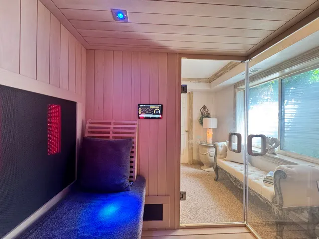 Custom sauna featuring wood paneling, built-in bench seating, integrated lighting, and a glass entry door