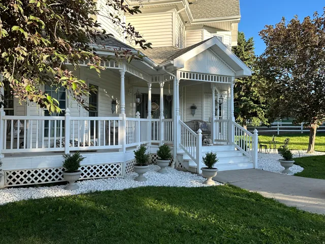 Inviting Victorian-style front porch with white railings and lattice skirting, featuring a gabled entryway and exterior wall sconces