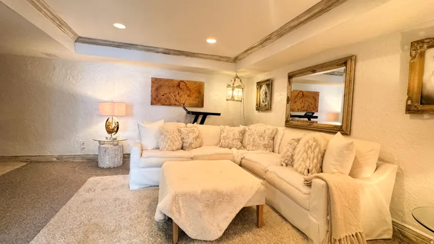 Recessed lighting illuminates a carpeted living space with textured walls and ceiling beams