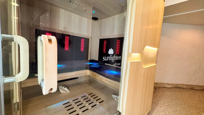 Integrated sauna featuring a glass door, light wood paneling, built-in bench seating, and interior lighting