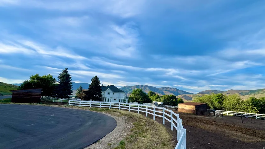 Expansive property featuring a white picket fence, a large barn structure, an asphalt drive, and mature trees