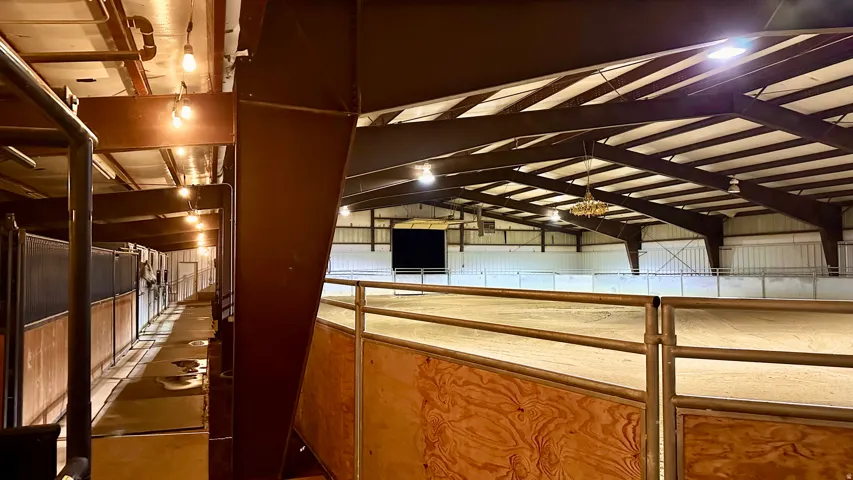 Indoor riding arena featuring overhead lighting, a sand footing surface, and a substantial steel-frame structure
