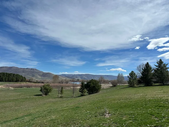 Expansive green lawn sloping towards a body of water, bordered by distant mountains