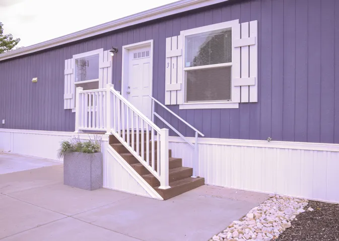Exterior featuring vertical panel siding in a blue tone, white trim, and a white entry door with an overhead light fixture