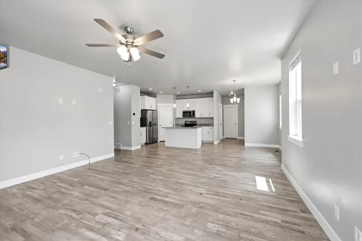 Open-concept living space featuring wood-finish flooring, a ceiling fan with integrated lighting, and multiple windows