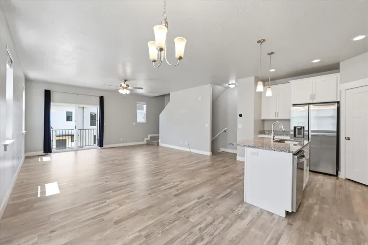 Open-concept living area featuring wood-finish flooring, a kitchen island with stone countertop, stainless steel appliances, white cabinetry, and a sliding glass door leading to an exterior balcony