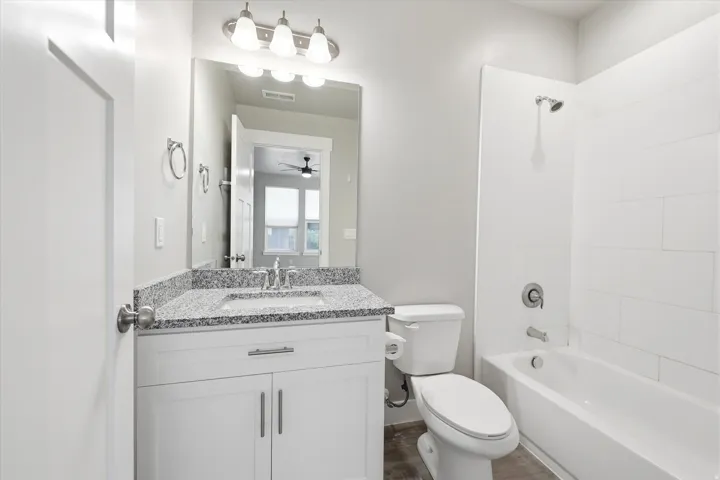 Bathroom featuring a white vanity with a speckled countertop, a large mirror, and a full bathtub with white subway tile surround