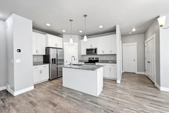 Kitchen featuring white cabinetry, stainless steel appliances, granite countertops, a center island with sink, and wood-finish flooring