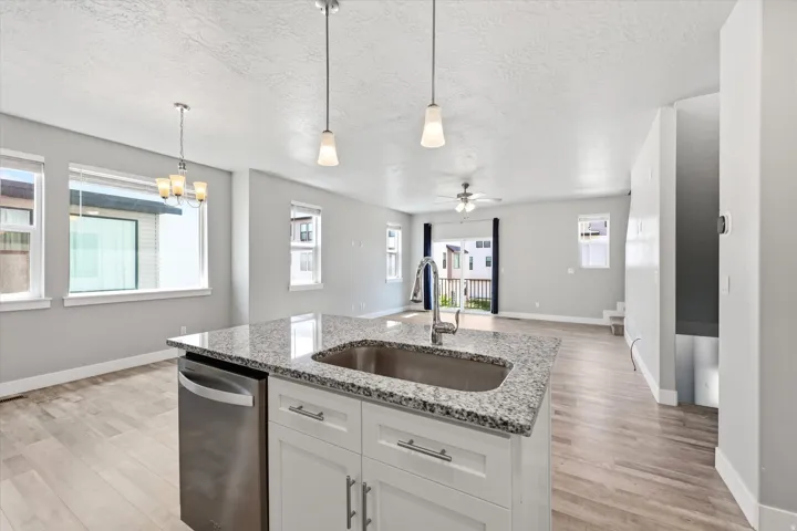 Spacious open-concept living area featuring a kitchen island with a granite-style countertop, integrated stainless steel dishwasher, and a stainless steel sink with a gooseneck faucet