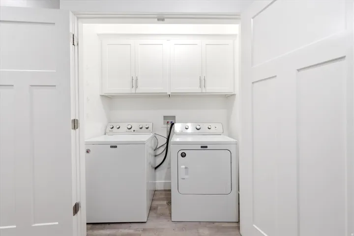 Dedicated laundry area featuring a washer and dryer, upper cabinetry for storage, and wood-finish flooring