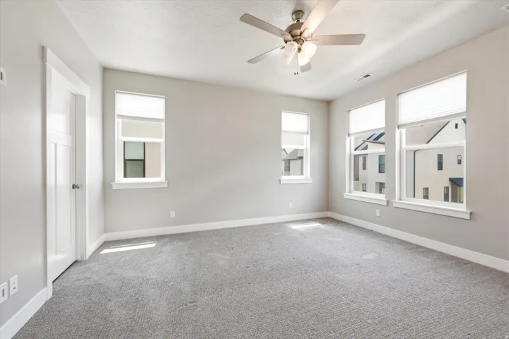 Carpeted room featuring multiple windows, a ceiling fan with light fixture, and a paneled interior door