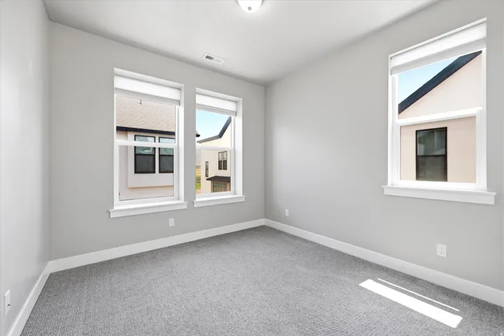 Neutral gray walls with white trim, gray carpet flooring, and multiple windows with white roller shades