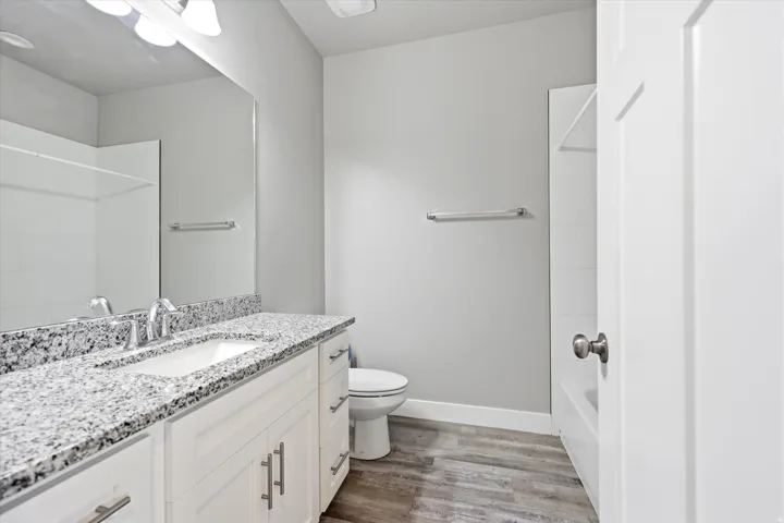 Bathroom featuring a white vanity with brushed nickel hardware, a speckled countertop, a single undermount sink with a chrome faucet, and wood-finish flooring