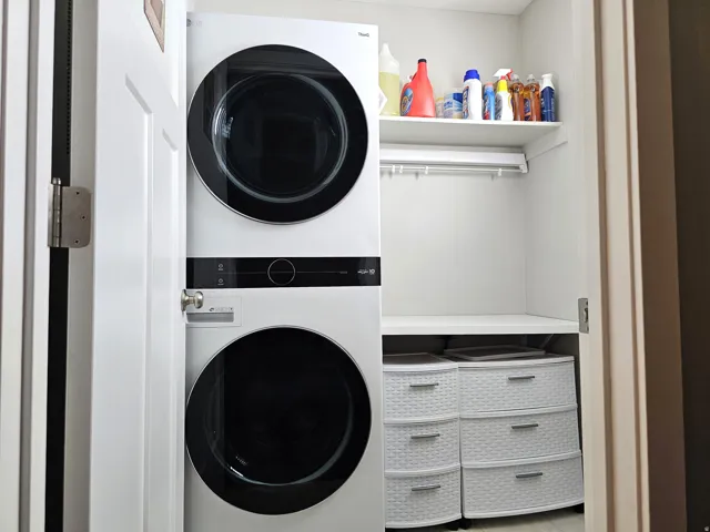 Dedicated laundry closet with a stacked washer and dryer, integrated shelving, and a built-in hanging rod