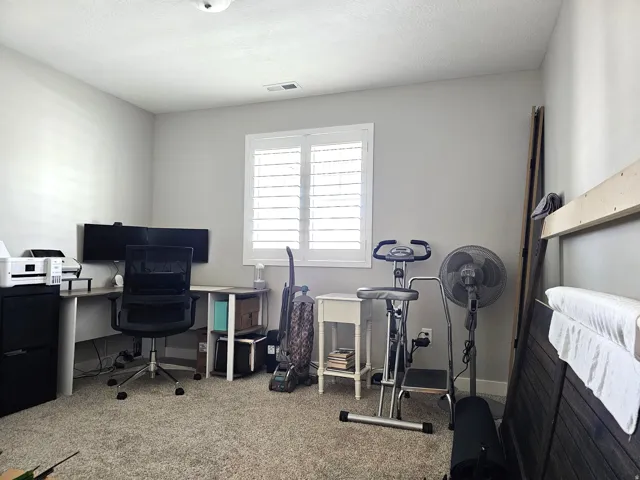 Carpeted room with a window featuring white plantation shutters
