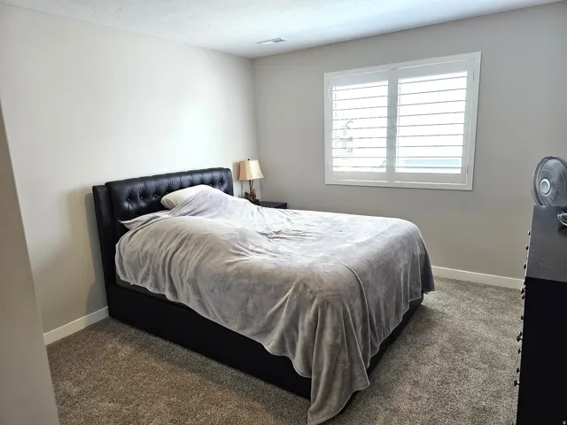 Carpeted room with a window featuring white plantation shutters, light-colored walls, and white baseboards