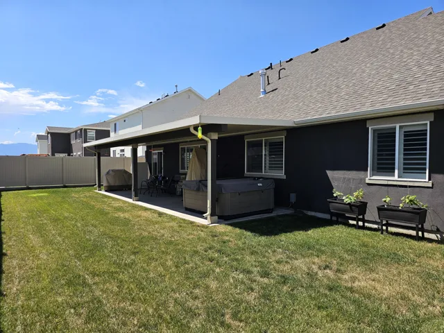 Expansive backyard featuring a covered patio, manicured lawn, and privacy fencing