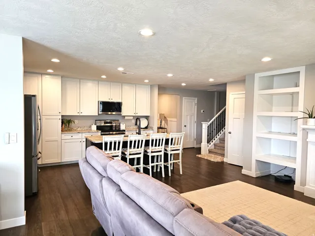 Open-concept living space featuring a modern kitchen with white cabinetry, stainless steel appliances, and a central island with seating