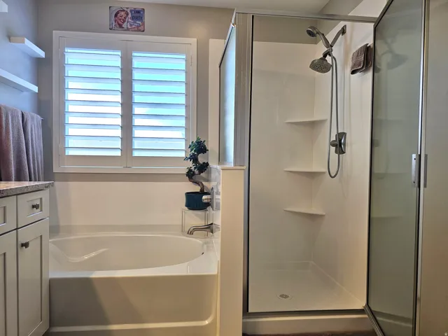 Bathroom featuring a built-in soaking tub, walk-in shower with glass enclosure, dual shower heads, and white plantation shutters