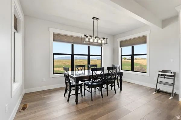 Spacious dining area featuring wood-finish flooring, ample natural light from multiple large windows, and a modern linear chandelier