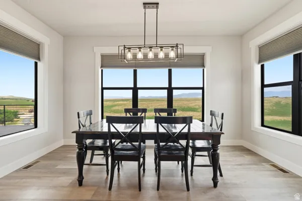 Bright dining area featuring a linear chandelier, wood-finish flooring, and expansive windows