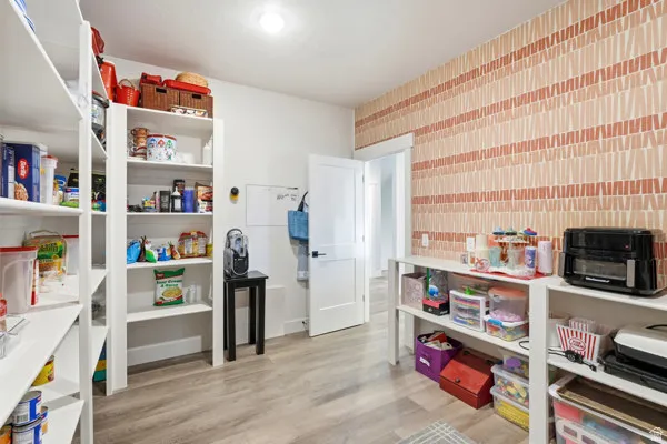 Spacious utility room featuring extensive built-in shelving, wood-finish flooring, a patterned accent wall, and a white interior door