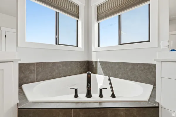 Corner soaking tub with a dark bronze faucet, surrounded by tiled walls and a tiled tub deck