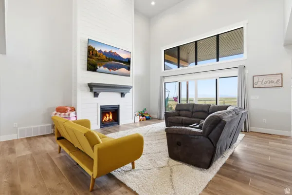 Great room featuring a shiplap-clad fireplace with a dark wood mantel, wood-finish flooring, high ceilings with recessed lighting, and expansive windows