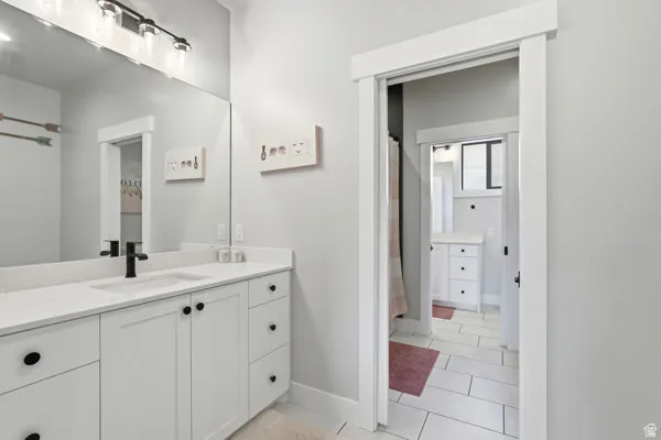 Bathroom featuring a large vanity with white cabinetry, a light-toned countertop, and a rectangular undermount sink with a matte black faucet