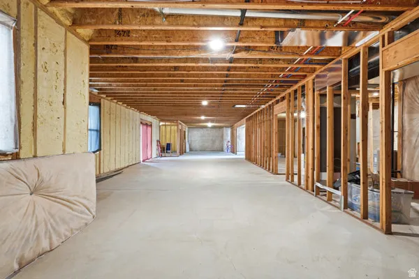 Unfinished basement featuring exposed wood framing, concrete flooring, visible insulation, and overhead lighting