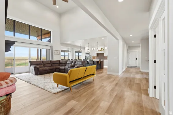 Open-concept living space featuring high ceilings, wood-finish flooring, a full wall of glass with sliding door access, and an integrated kitchen with an island