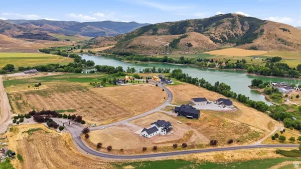 Expansive land parcels featuring paved road access, scattered new construction homes, and a prominent river frontage, all set against a backdrop of rolling hills and distant mountains