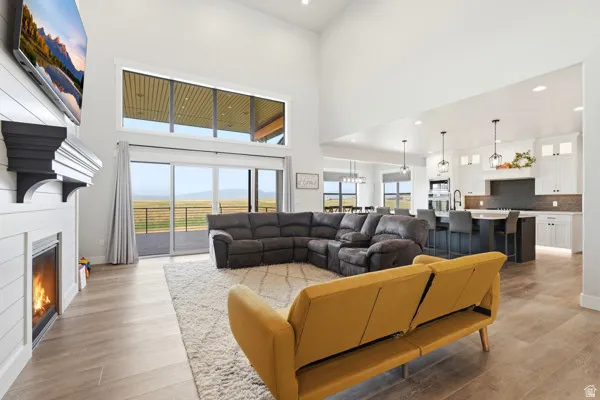 Open-concept living space featuring high vaulted ceilings, large glass sliding doors, wood-finish flooring, and a fireplace with a shiplap surround