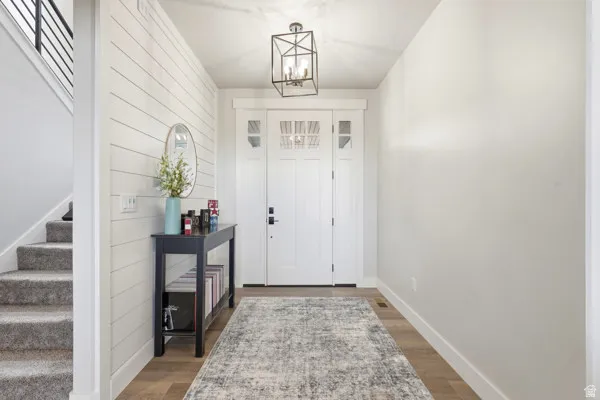 Entryway featuring wood-finish flooring, shiplap accent wall, and a staircase with carpeted treads and metal balusters