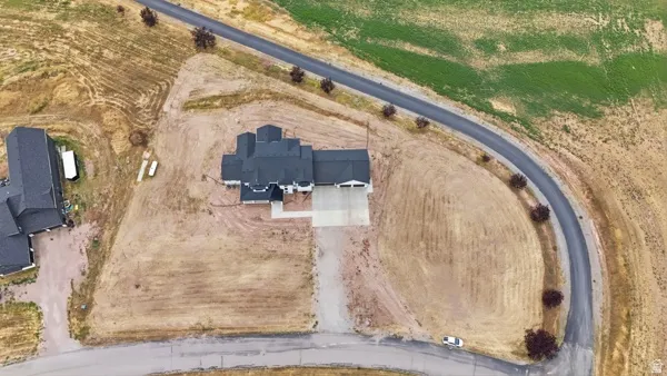Expansive property featuring a newly constructed residence with a dark roof, a concrete driveway, and surrounding undeveloped land