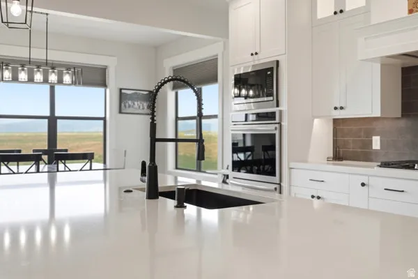Spacious kitchen featuring a large island with an undermount sink and matte black pull-down faucet, white shaker cabinetry with dark hardware, stainless steel built-in appliances, and a gray subway tile backsplash