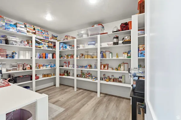 Expansive pantry featuring extensive built-in white shelving, wood-finish flooring, and recessed ceiling lighting