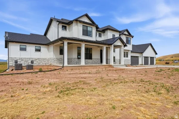Modern farmhouse exterior featuring white board-and-batten siding with stone veneer accents, a dark shingle roof, and a covered front porch with substantial columns