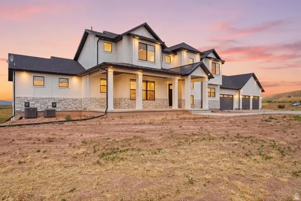 Modern farmhouse exterior featuring board and batten siding, stone accents, a covered entry porch with columns, a dark shingle roof, and multiple garage doors