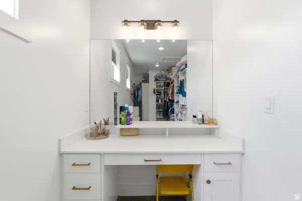 Built-in vanity area featuring white cabinetry, gold-finish hardware, a large wall-mounted mirror, and a three-light fixture